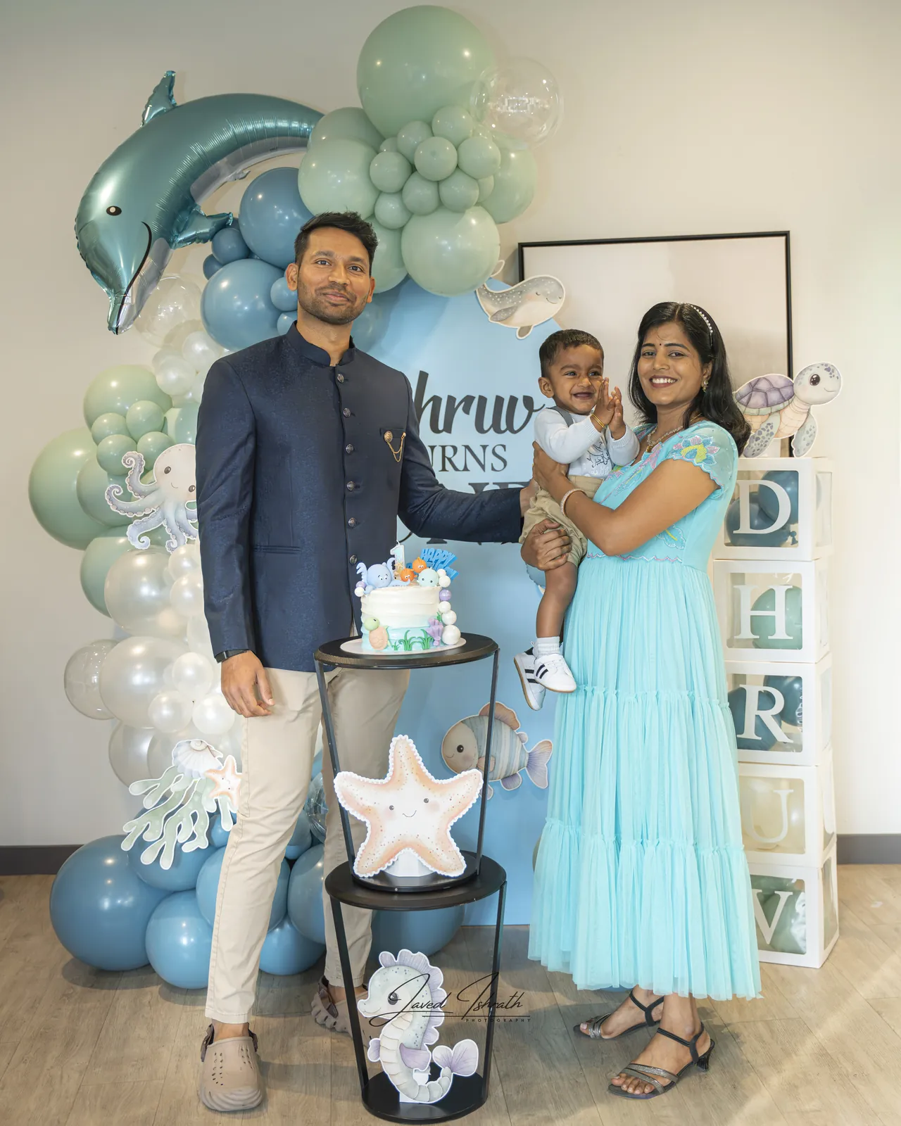 A family posing by a balloon backdrop at a first birthday